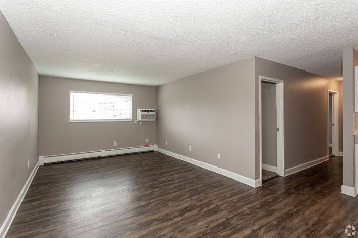 Spacious living room with elegant dark hardwood floors and soft gray walls, featuring bright natural light from large window, perfect for cozy gatherings.