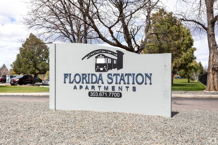 Inviting sign for Florida Station Apartments, set against a picturesque backdrop of trees and clear skies.