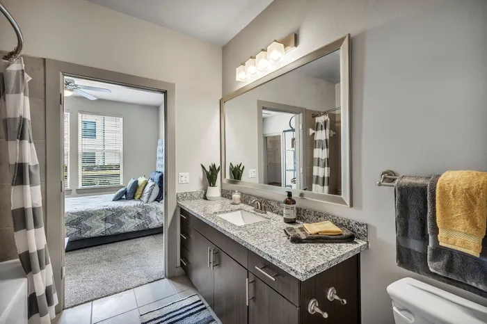 Chic bathroom with granite countertop, elegant mirror, and cozy bedroom view, showcasing modern apartment living.