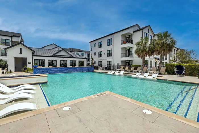 Inviting poolside view of a stylish apartment complex, featuring a sparkling swimming pool, comfortable loungers, and elegant architecture, ideal for luxurious living.