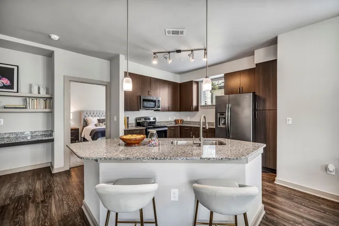 Modern kitchen with granite countertops, stainless steel appliances, and cozy bar seating. Open layout with a glimpse of a chic bedroom, highlighting elegant design and comfort.