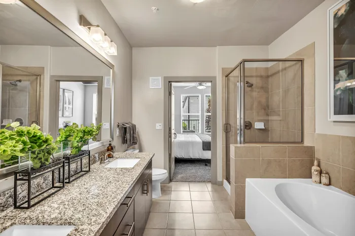 Luxurious bathroom with elegant granite countertops, dual sinks, and a spacious shower, leading into a bright bedroom with natural light.