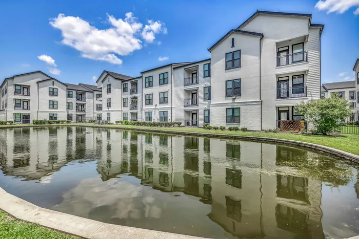 Charming modern apartment complex with beautiful water views, landscaped greenery, and elegant architecture under a bright blue sky.