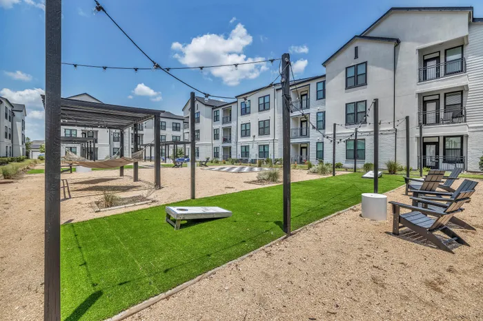 Charming apartment community with vibrant outdoor social space, featuring cozy hammocks, string lights, and a cornhole game area.