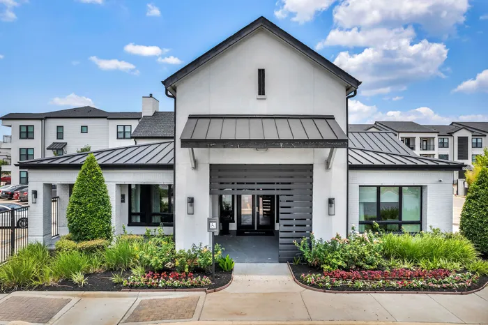 Modern apartment building entrance with stylish architecture, lush landscaping, and clear blue skies.