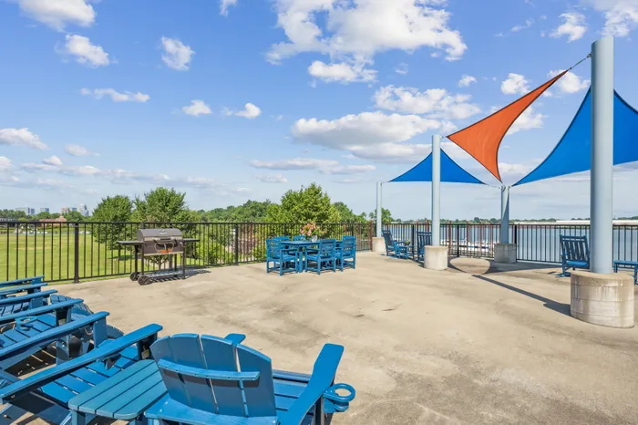 Inviting rooftop patio with vibrant blue seating and a barbecue grill, under colorful shade sails overlooking scenic views.