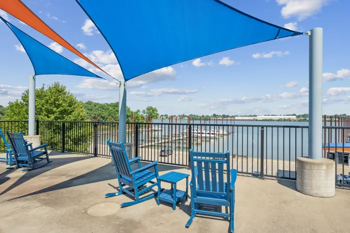 Scenic waterfront patio with vibrant blue shade sails and comfortable seating, offering a tranquil view of the marina on a sunny day.
