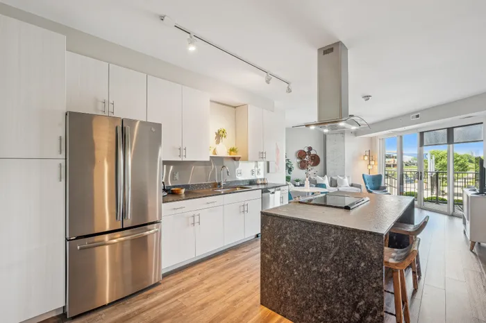 Chic modern kitchen with sleek stainless steel appliances, island seating, and open-concept living area leading to a sunny balcony.