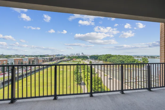 Stunning urban balcony view showcasing lush green spaces and serene waterfront against a vibrant blue sky.