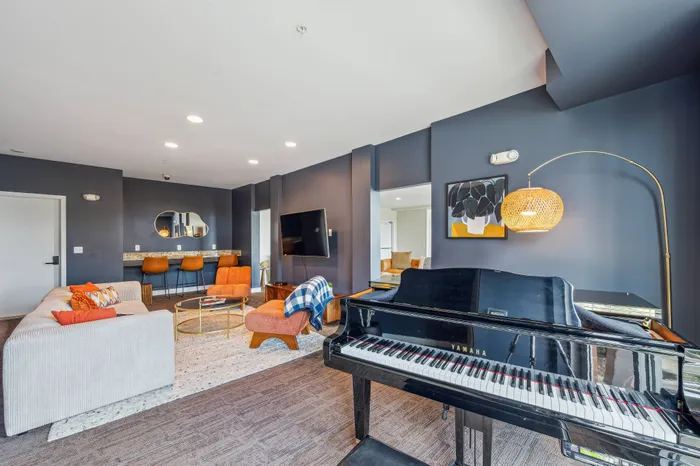 Chic living room with elegant piano, modern decor, plush sofas, and vibrant orange accents creating a stylish and inviting ambiance.