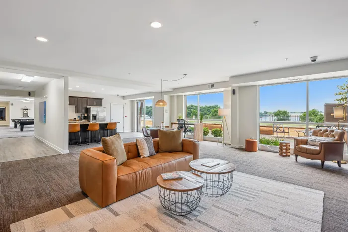 Bright, open-concept living space with plush seating, modern kitchen, and panoramic floor-to-ceiling windows overlooking lush greenery.