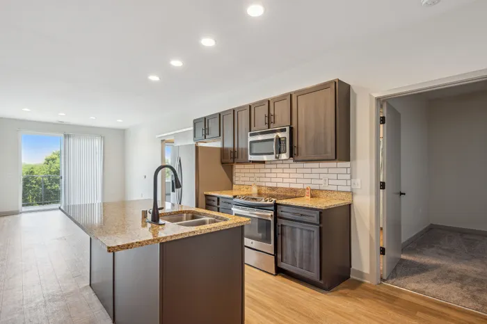 Modern kitchen with granite countertops, stainless steel appliances, and a spacious island, seamlessly opening into a bright living area with scenic views.