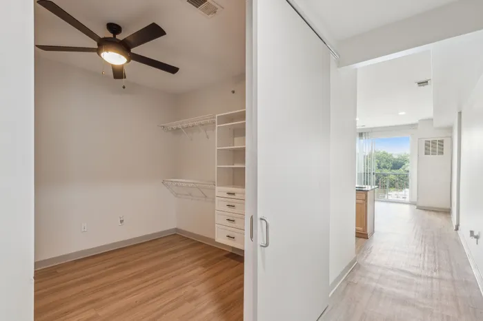 Bright hallway view featuring sleek wooden floors, modern ceiling fan, and spacious closet in a chic apartment.