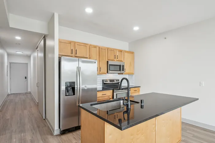 Modern kitchen with sleek stainless steel appliances, elegant black countertop island, and warm wooden cabinets.