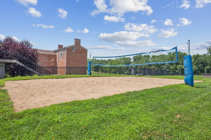 Charming brick building with an adjacent sand volleyball court, set against a lush green landscape and blue skies.