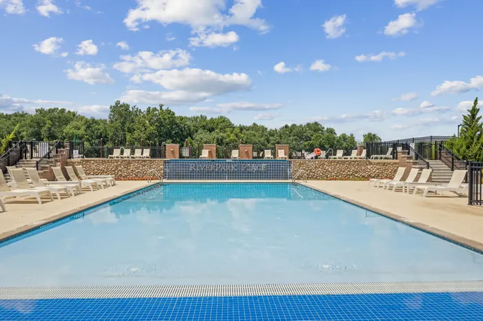 Inviting outdoor pool at Riverpark Place surrounded by sun loungers and lush green trees under a clear blue sky.