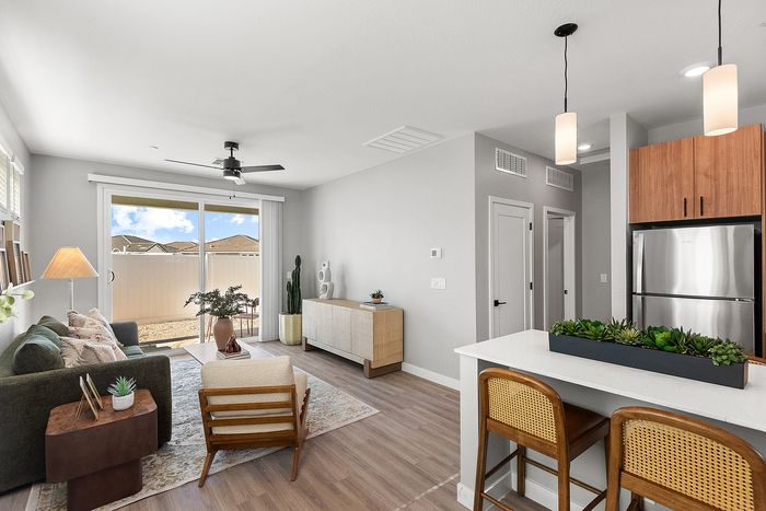 Bright and modern living space with an open layout, featuring sleek kitchen bar, cozy seating area, and large sliding doors leading to a sunny patio.
