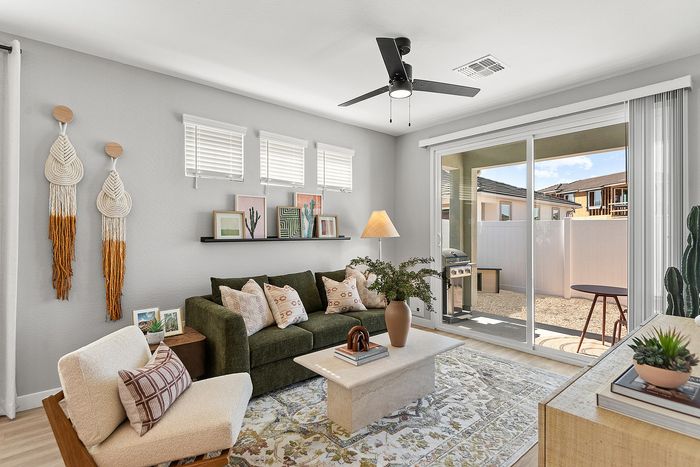 Bright and inviting living room with modern decor, featuring a cozy green sofa, stylish wall art, and a large sliding glass door opening to a charming outdoor space with a barbecue area.