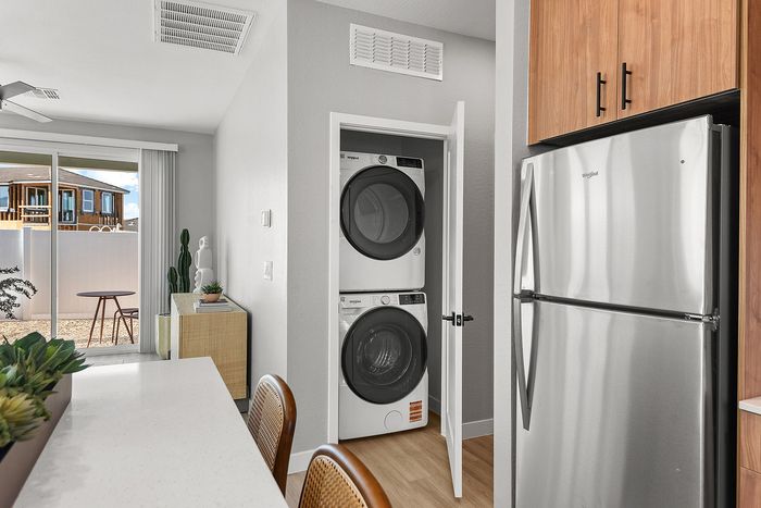 Modern apartment kitchen with sleek stainless steel fridge, in-unit stacked washer-dryer, and a bright open space leading to patio with large sliding doors.