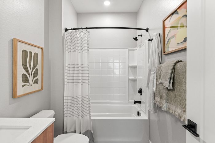 Elegant bathroom with modern fixtures, featuring a sleek white shower, stylish curtain, and tasteful artwork.