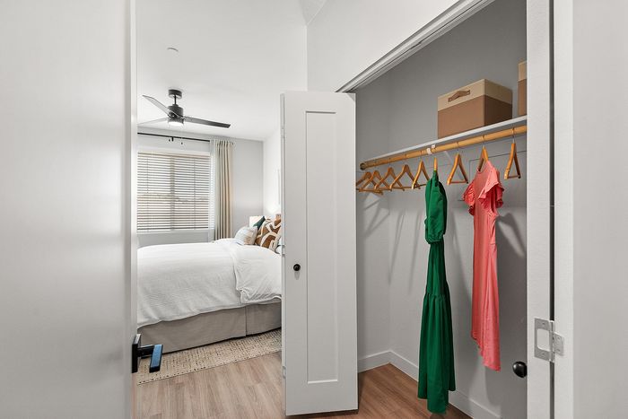 Bright bedroom with cozy white bedding, expansive closet with elegant dresses, and sleek ceiling fan, perfect for stylish living.