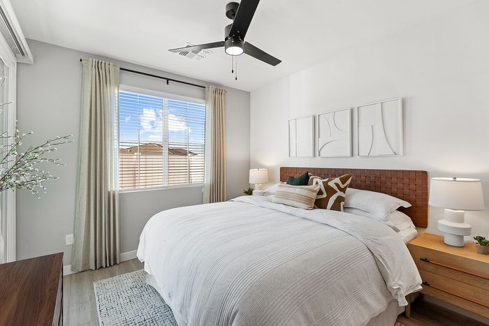 Inviting bedroom with a cozy king-size bed, stylish decor, natural light streaming through large windows, and a contemporary ceiling fan.