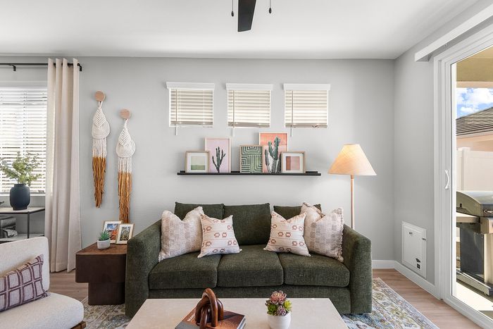 Chic living room with a stylish green sofa, cozy cushions, modern wall art, and warm natural light pouring in through large windows.