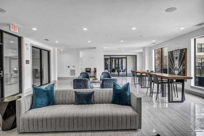Modern apartment lounge with sleek gray sofa, blue accent pillows, and spacious seating area featuring stylish furniture and natural light.