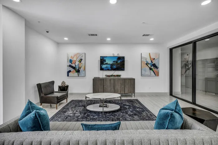 Modern living room with elegant decor, featuring abstract art, plush blue cushions, and a sleek entertainment setup.