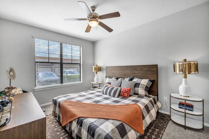 Inviting bedroom with modern decor, featuring a checkered bedspread, stylish lamps, and natural light through large windows.