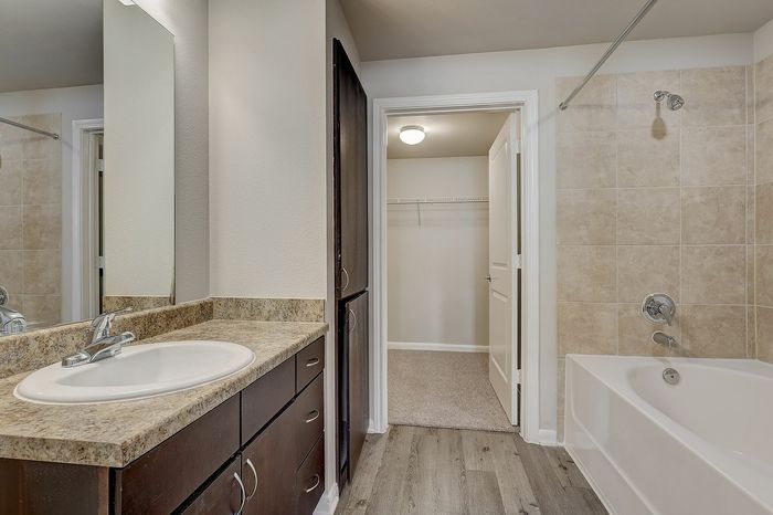Modern bathroom with elegant granite countertops, spacious vanity, and a clean tile bathtub, leading to a bright walk-in closet.