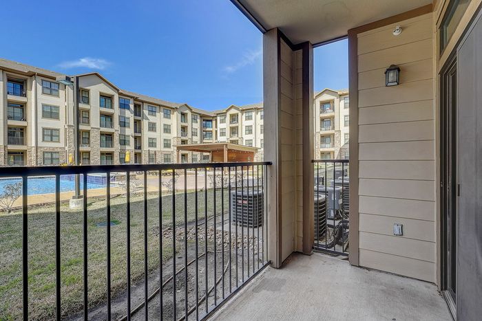 Charming apartment balcony overlooking a lush courtyard and inviting pool, perfect for relaxation and outdoor enjoyment.