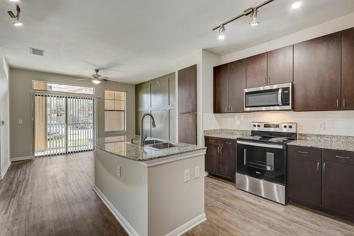 Modern kitchen featuring sleek granite countertops, stainless steel appliances, and elegant dark wood cabinetry with ample natural light.