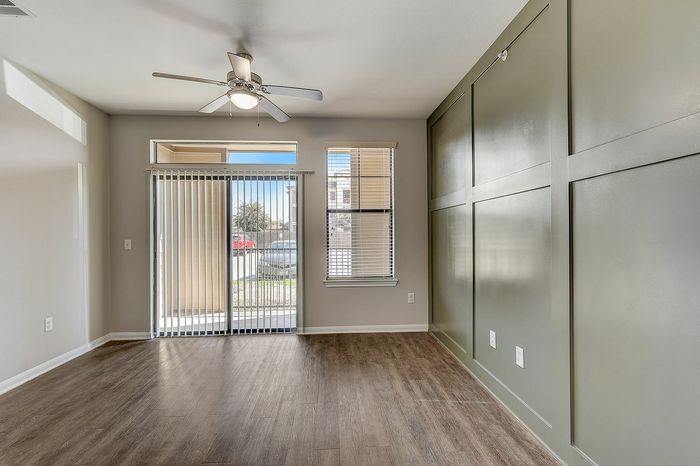 Bright and inviting living space with sleek hardwood floors, elegant green accent wall, and abundant natural light through large windows and sliding glass door.