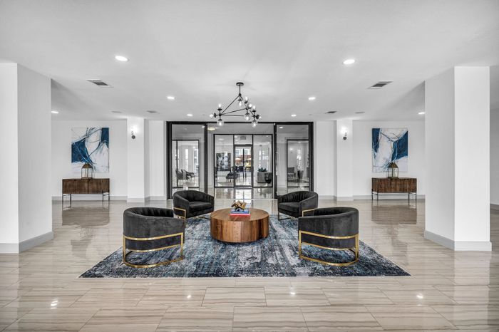 Elegant and modern lobby featuring sleek armchairs, a chic chandelier, and stylish artwork, set on polished flooring.
