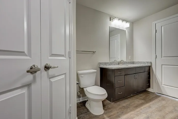 Modern bathroom with sleek granite countertop, elegant cabinetry, and pristine white fixtures, enhanced by stylish flooring and ample lighting.