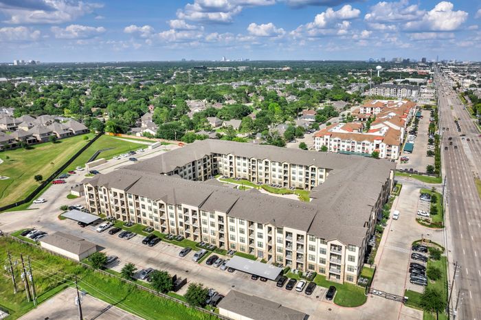 Expansive aerial view of a charming residential apartment complex surrounded by lush greenery and well-maintained parking areas, set in a vibrant suburban neighborhood.