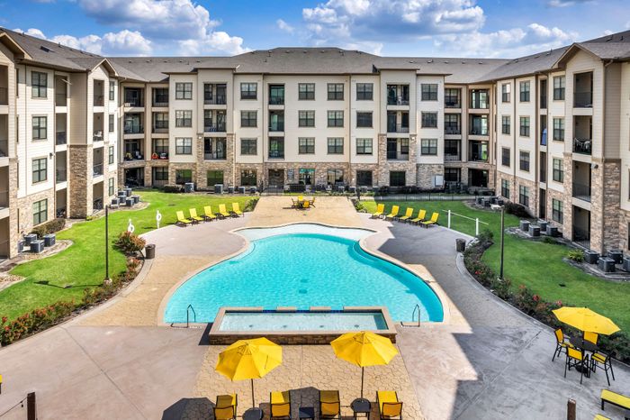 Luxurious apartment complex showcasing a stunning central pool, surrounded by green spaces and bright yellow lounge chairs, perfect for relaxation under the sun.
