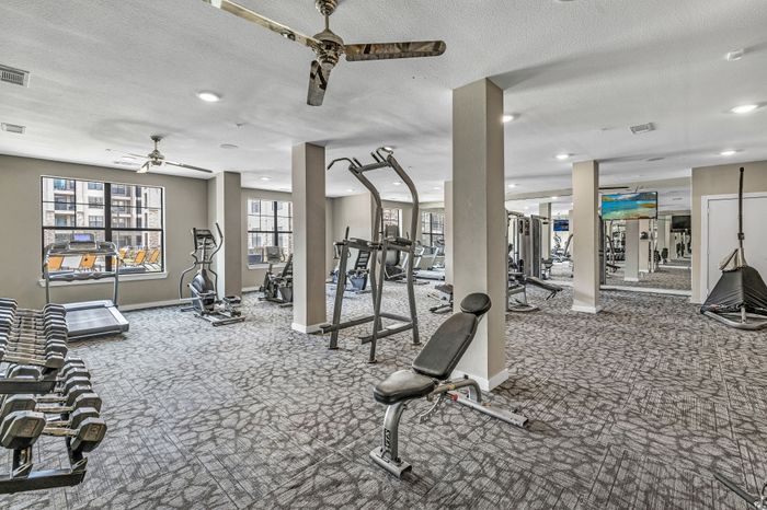 Modern fitness center with natural light featuring treadmills, weight benches, and exercise equipment for an active lifestyle.