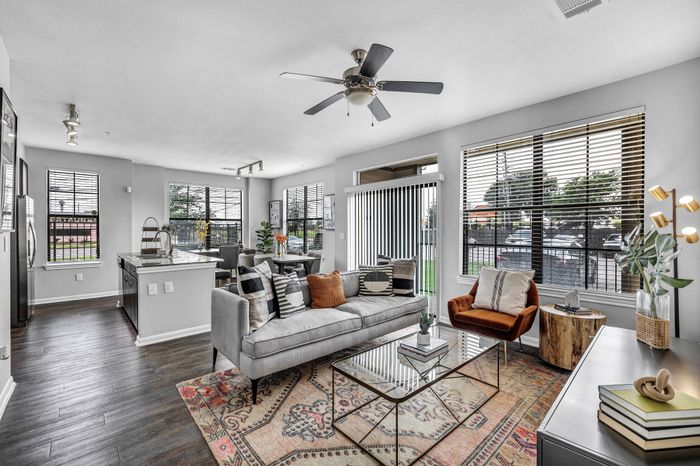 Chic open-plan living room with elegant decor, featuring a modern kitchen, stylish gray sofa, and cozy armchair, flooded with natural light from large windows.