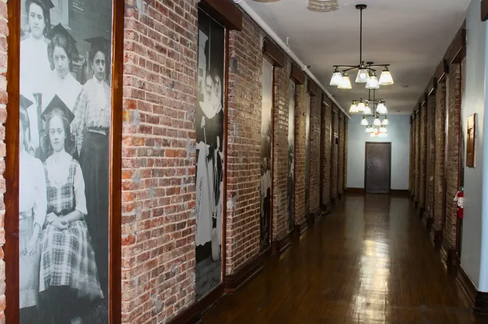 Charming brick corridor adorned with vintage photographs, under elegant lighting fixtures, offering a blend of history and modernity.