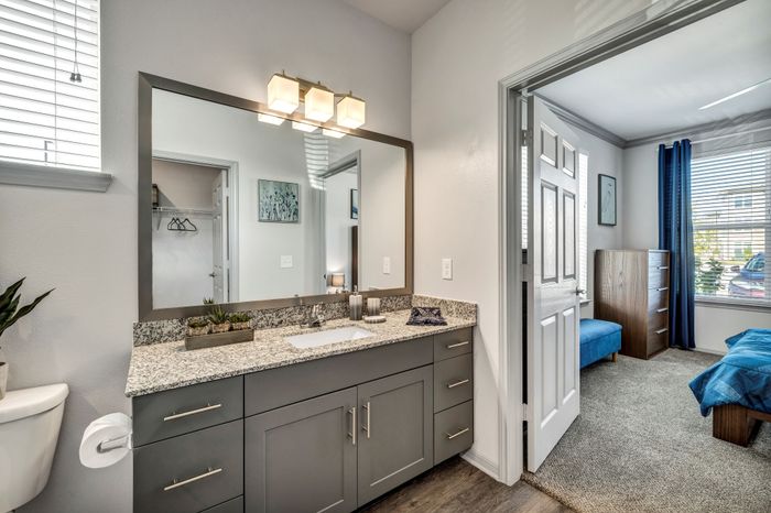 Modern bathroom with elegant granite countertop, large mirror, and a view into a cozy bedroom with stylish blue accents.