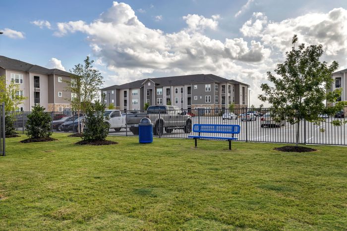 Charming apartment complex with well-maintained grounds, featuring a lush green area and inviting blue bench under a vibrant sky.