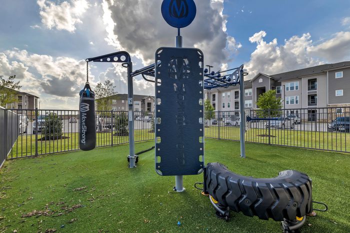 Modern outdoor gym with versatile workout equipment set against a backdrop of contemporary apartment buildings under a bright sky.