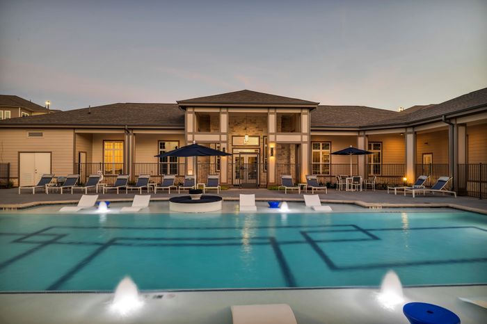 Elegant apartment complex with a stunning resort-style pool, spacious lounging areas, and ambient evening lighting creating a serene outdoor experience.