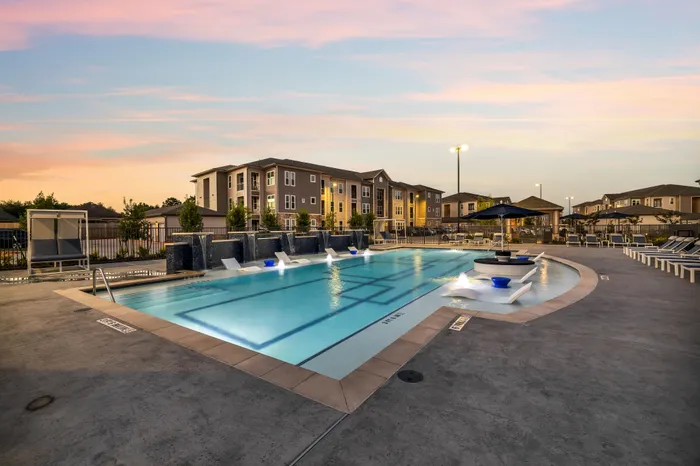 Luxurious apartment complex with a stunning outdoor pool and elegant poolside lounge chairs at sunset.