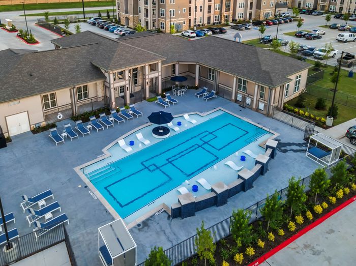 Luxurious apartment complex showcasing a stunning outdoor pool with stylish lounge chairs and greenery, perfect for relaxation.