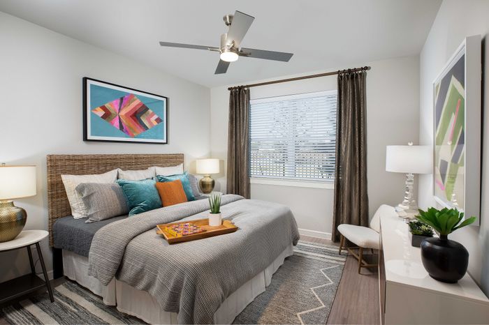 Chic bedroom with woven headboard, cozy bedding, and contemporary artwork, featuring natural light and stylish decor.