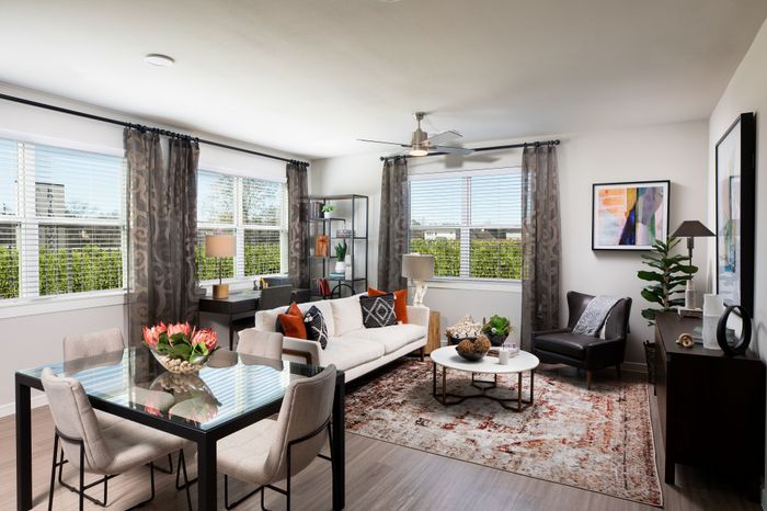 Bright and elegant living room with modern decor, featuring a cozy white sofa, stylish chairs, and a glass-top dining table, bathed in natural light from large windows.