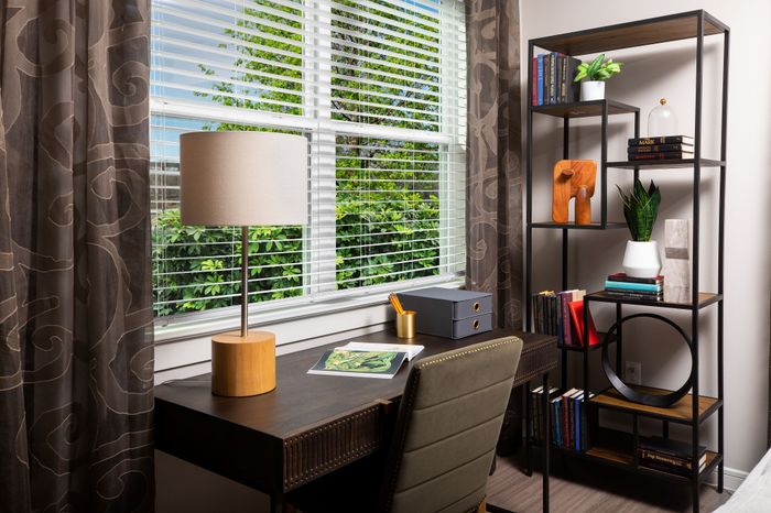 Bright and inviting home office space featuring a stylish desk with a modern lamp, a comfortable chair, and an organized bookshelf by a large window with lush garden views.